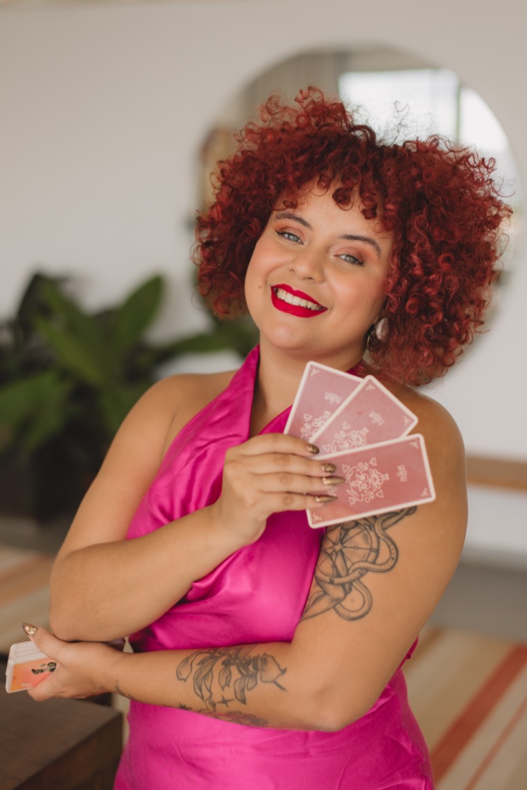 Amanda, cartomante d'O Tarô de Amanda, sorrindo e segurando cartas de Tarô